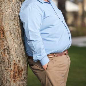 Side view of an overweight mature man leaning on a tree, mid section, close-up. Focus on the model. Square composition. Image taken with Nikon D800 and developed from Raw format.